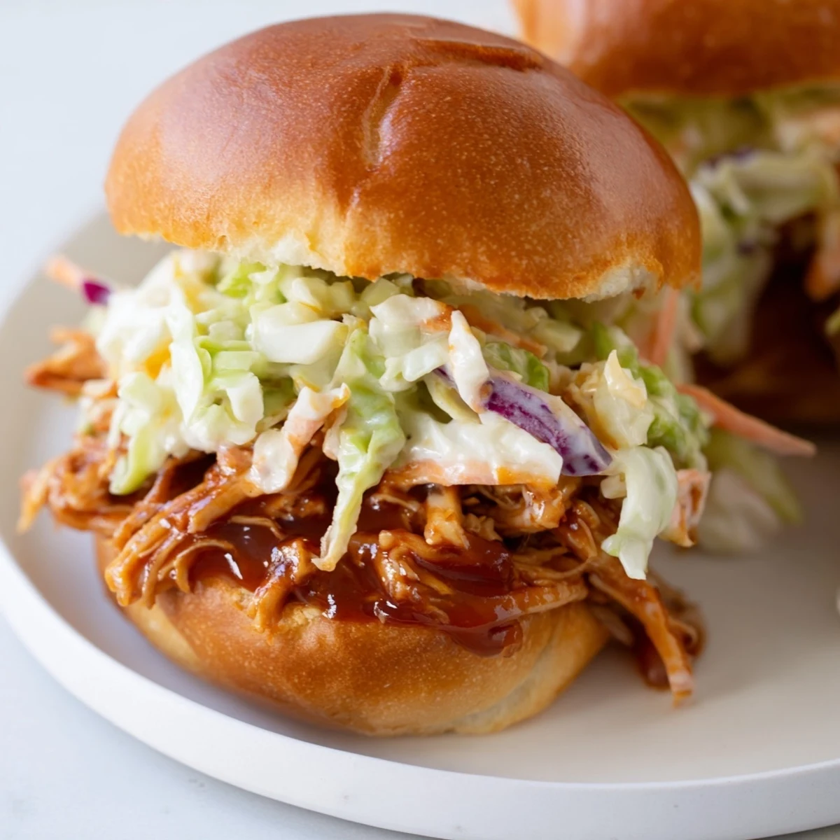 Mini BBQ Chicken Sliders sit on a platter, featuring tender pulled chicken and crunchy slaw in toasted buns, perfect for game day parties.