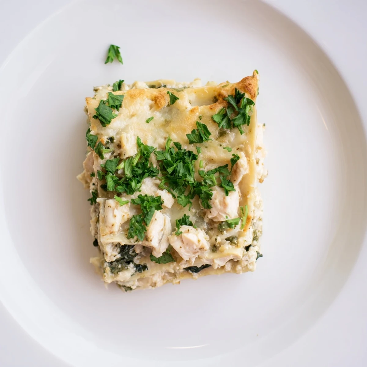 Fresh spinach and shredded chicken peek through creamy Alfredo sauce between lasagna noodles in this savory Italian-inspired casserole.