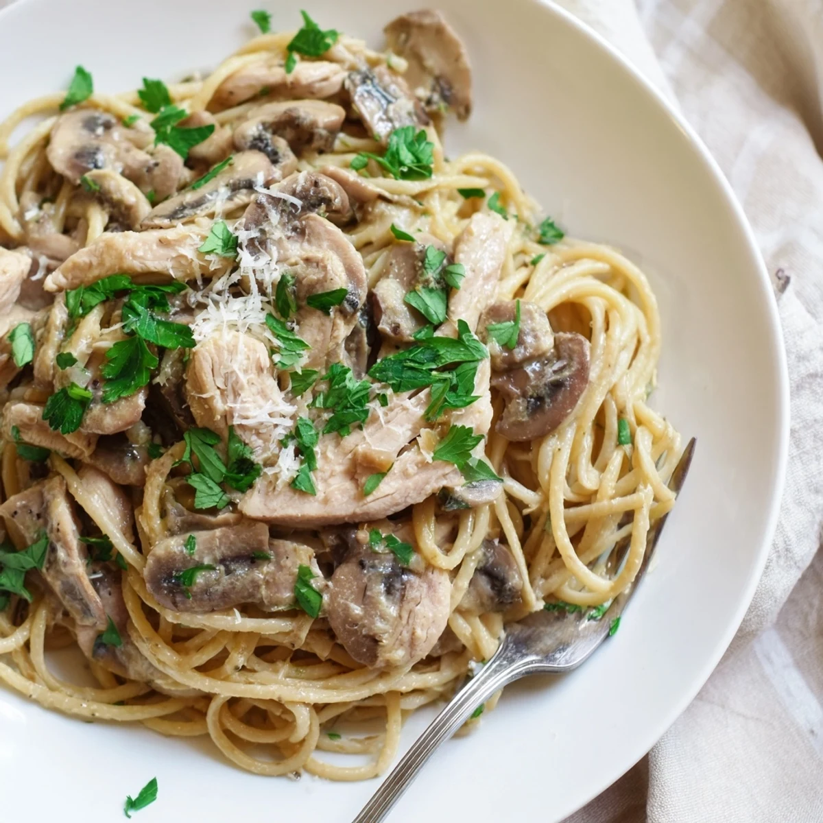 Golden-brown sliced chicken breast and al dente whole wheat spaghettini coated in a creamy mushroom Parmesan sauce, garnished with fresh parsley.