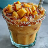 A refreshing alcohol-free mango drink layered with spicy-sweet Tajín and fresh diced mango, served in festive glasses.