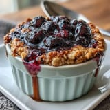 Warm, single-serve baked oats with fresh blueberries, maple sweetness, and a soft, comforting texture in a rustic ramekin.