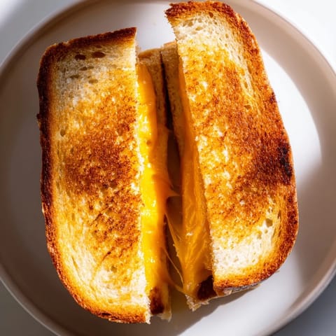 A close-up of a perfectly toasted Mayo Grilled Cheese, oozing with melted cheddar cheese.