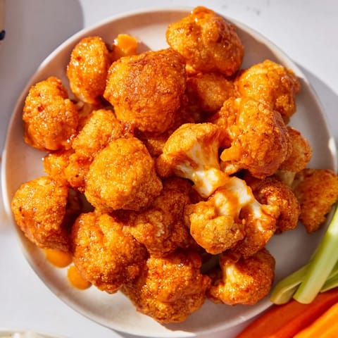Vibrant plate of Buffalo Cauliflower Bites, with celery sticks and creamy ranch for dipping and fun.