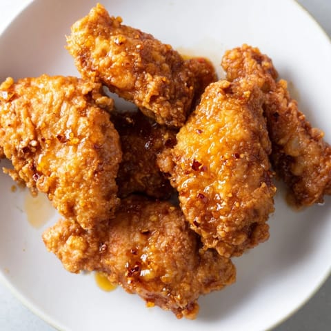 Golden-brown fried chicken thighs glistening with a sweet and spicy hot honey butter sauce on a rustic plate.