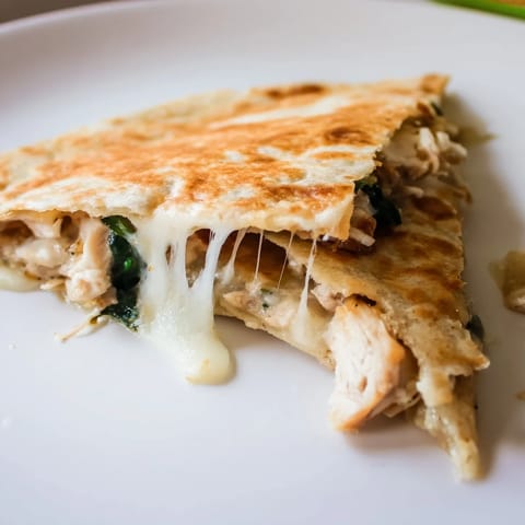 A close-up of a Chicken and Spinach Quesadilla revealing juicy shredded chicken, vibrant wilted spinach, and gooey cheese between golden tortilla folds.  