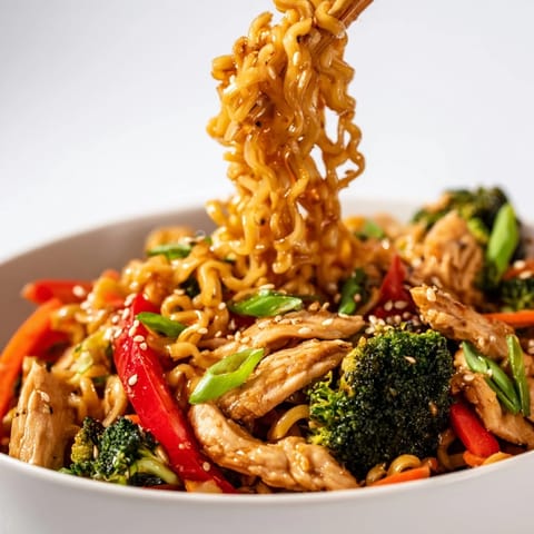 A close-up of a steaming bowl of Spicy Ramen Stir-Fry, garnished with fresh cilantro, sesame seeds, and sliced green onions.