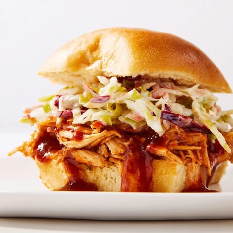 A close-up of BBQ Chicken Sliders shows juicy, saucy shredded meat and vibrant slaw spilling from soft mini buns, ready to serve.