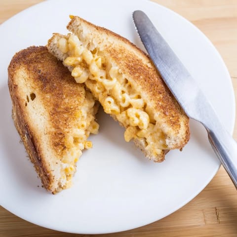 Steaming melted cheddar oozes from a crispy Mac & Cheese Grilled Cheese served on a checkered plate.