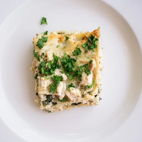 Fresh spinach and shredded chicken peek through creamy Alfredo sauce between lasagna noodles in this savory Italian-inspired casserole.