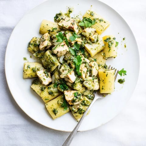 Grilled chicken slices rest on penne pasta, generously coated in vibrant, herb-packed chimichurri sauce for a fresh, zesty fusion meal.