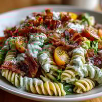 A colorful bowl of BLT pasta with avocado ranch, featuring crispy bacon, fresh lettuce, and juicy cherry tomatoes tossed in creamy dressing.